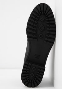 Semelle extérieure en caoutchouc noir avec une texture antidérapante présentant des motifs en diamants et rectangulaires. La marque TOMS est embossée sur le côté.