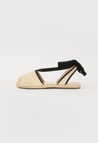 Bežinės espadrilės su paminkštintu, apvaliu pirštu, juodais dirželiais ir pintu džutiniu padu. Minimalistinio dizaino su angomis oro pralaidumui.