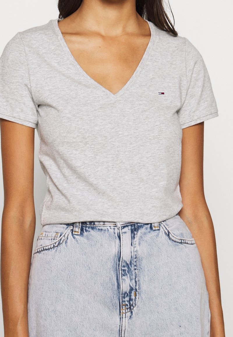 Grå kortärmad tröja med V-hals, tillverkad av mjuk bomull, med en liten logga på vänster bröst och en figursydd design.