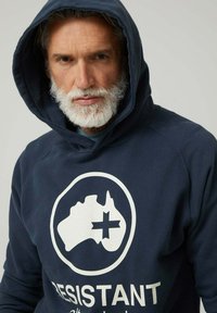 Sudadera con capucha azul marino hecha de tela suave, con un gran gráfico blanco de Australia y la palabra "RESISTENTE" en letras negritas.
