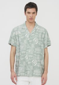 Camicia a maniche corte con bottoni di colore verde chiaro e modelli geometrici bianchi. Presenta un colletto allargato e una vestibilità morbida.