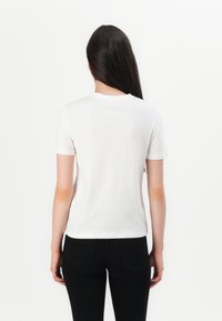 T-shirt en coton blanc à manches courtes, col rond et design ajusté, associé à un pantalon noir, vu de derrière.