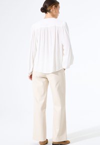 Witte textuurblouse met lange mouwen, met een losse pasvorm en een geplooide achterkant. Gepaard met beige wijde broekspijpen en bruine schoenen.