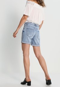 Ljusblå jeansshorts med uppvikta fållar, med en avslappnad passform, bakfickor och slitna detaljer, kombinerade med en vit off-shoulder-topp.