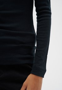 Svart långärmad topp i ett mjukt, stretchigt tyg. Har en slim fit med subtila sömdetaljer och en rundad fåll. Lämplig för lager-på-lager.