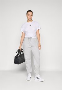 Bela kratka majica s kratkimi rokavi in črnim Adidasovim logotipom, sivi trenirke z vrvico, bele superge in črna športna torba.