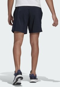 Pantalones cortos deportivos azul marino de corte relajado, fabricados con un tejido ligero, con bolsillos laterales y una textura suave, combinados con zapatillas de correr azul marino.