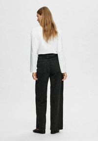 Jeans neri a vita alta e gamba larga con cintura, tasche posteriori e una leggera texture. Abbinati a una camicia bianca a maniche lunghe e scarpe basse.
