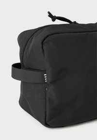 Pravoangularna crna najlonska torba s teksturiranom površinom, koja ima zatvarač i bočni remen. Minimalistički dizajn, bez vidljivih uzoraka ili logotipa.