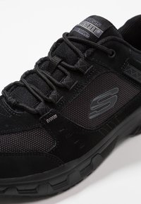 Chaussure de sport noire, alliant un cuir suédé lisse et des matériaux en mesh, avec une semelle texturée et un marquage bien visible sur le côté.