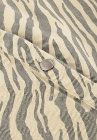 Tessuto a fantasia zebra in tonalità beige e grigie, con un dettaglio di bottone a pressione argento su una superficie testurizzata.