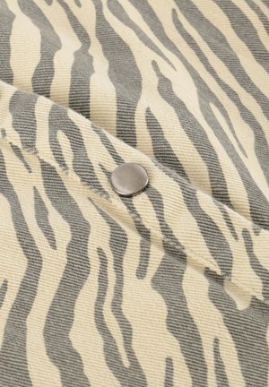 Tkanina z vzorom zebre v bež in sivi barvi z detajlom srebrnega snap gumbka na teksturirani površini.