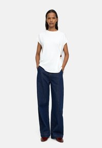 Biała bluzka z krótkim rękawem w połączeniu z szerokimi granatowymi dżinsami. Zauważalnym detalem jest mały ozdobny akcent z boku koszulki.