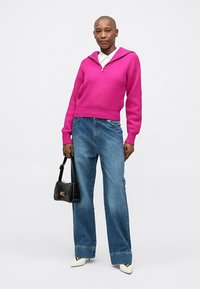 Fuchsia ribbad tröja med huva, kombinerad med ljusblå vida jeans, svart handväska och vita spetsiga skor. Enkelt och modernt utseende.