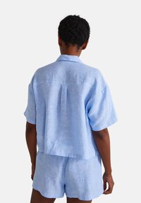 Chemise bleu clair à manches courtes en tissu texturé, avec une coupe décontractée et un pli dans le dos, associée à un short assorti.