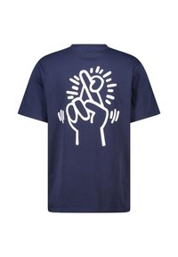 T-shirt en coton bleu marine avec un grand motif blanc représentant une main faisant un geste de "doigts croisés", agrémenté d'accents de rayons de soleil.