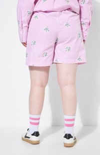 Pantaloni corti a righe rosa con motivi floreali verdi, abbinati a calze bianche con righe rosa e scarpe con accenti neri.