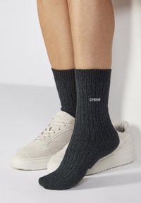 Graue gerippte Socken mit einem strukturierten Muster, an der Oberseite mit weißen Text "CPN H6N" versehen, kombiniert mit beigen Sneakers.