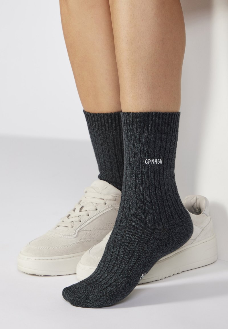 Graue gerippte Socken mit einem strukturierten Muster, an der Oberseite mit weißen Text "CPN H6N" versehen, kombiniert mit beigen Sneakers.