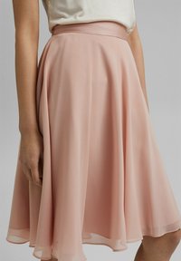 Ljusrosa, A-linjeformad kjol av genomskinligt tyg. Har en figurnära midja och ett flödande fåll, som visar upp en mjuk textur och ett mjukt rörelsemönster.