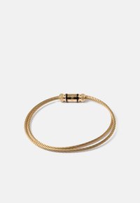 Bracelet en câble tressé doré avec un fermoir cylindrique comportant des accents noirs et le nom de la marque gravé "Guess."