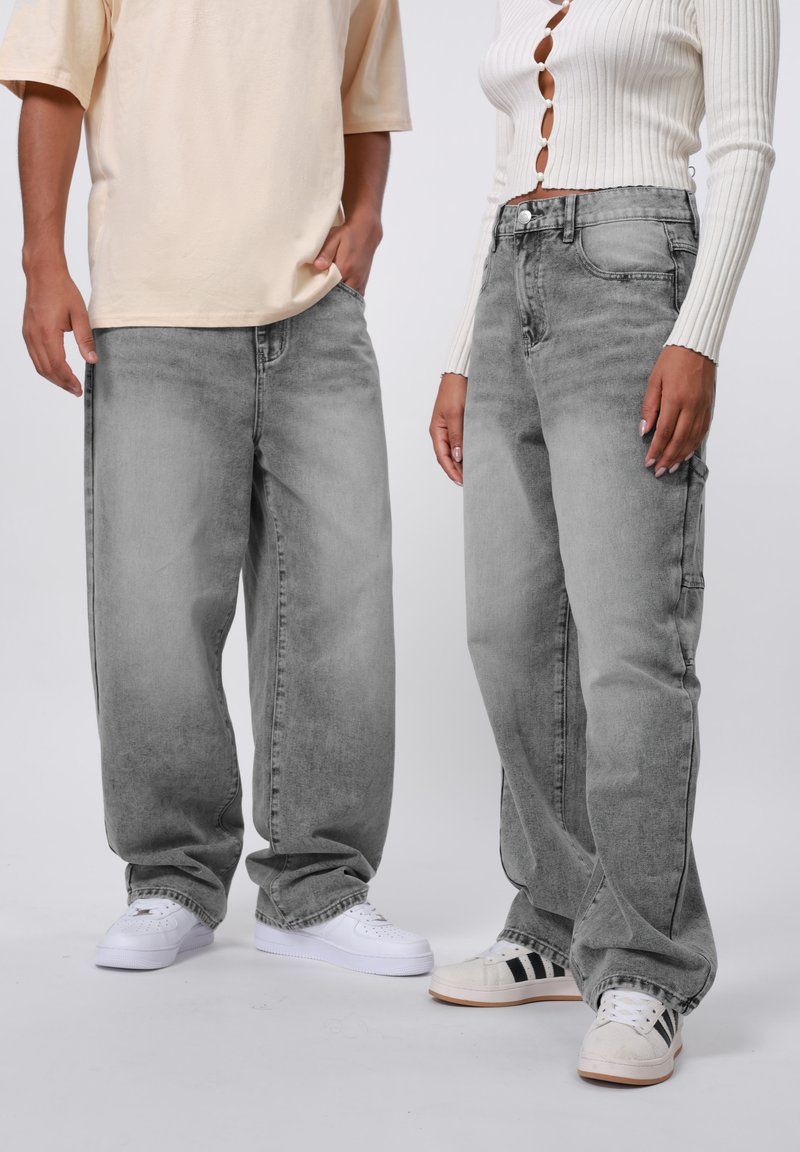 Vaqueros de mezclilla gris con un corte relajado, que presentan un acabado ligeramente desgastado y un diseño clásico de cinco bolsillos. Llevados con zapatos blancos y claros.
