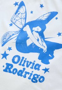 Modrá grafická tričko s návrhom motýlích krídel a sediacej postavy v modrom atramente. Text obsahuje "Olivia Rodrigo" a hviezdičkové akcenty na bielom pozadí.