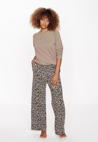 Maglia beige a maniche lunghe con una vestibilità rilassata, abbinata a pantaloni larghi con stampa leopardata nera e beige, dotati di tasche laterali e un morbido tessuto.