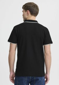 Svart polo skjorte med korte ermer, med grå aksentstriper på kragen og mansjettene, laget av et teksturert stoff.