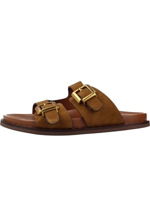 Sandalia tipo slide de ante marrón con dos tiras anchas con grandes hebillas doradas y suela plana.