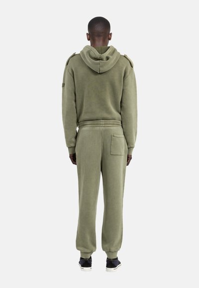 Olijfgroene hoodie en broek set, gemaakt van zachte stof. Bevat zijzakken, een patch op de schouder en aansluitende manchetten.