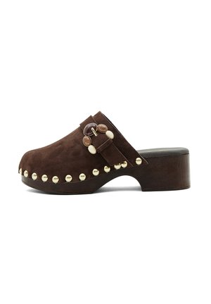 Bruine suède klomp met houten plateauhak, decoratieve gouden studs langs de zool en een bandje met ronde steenversieringen.