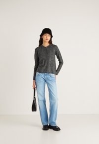 Siv pleteni dolg rokav z ovratnikom, kombiniran s svetlo modrimi kavbojkami z ravnim krojem. Dodatki vključujejo črno torbico in klobuk.