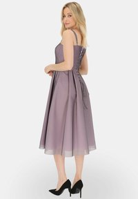 Jasnofioletowa satynowa sukienka na cienkich ramiączkach, dopasowana w górnej części, z rozkloszowanym dołem. Posiada ozdobne sznurowanie z tyłu oraz przezroczystą nakładkę.