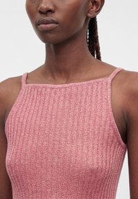 Gros plan d'une personne portant un top sans manches en maille côtelée rose avec de fines bretelles et des cheveux tressés visibles derrière l'épaule.