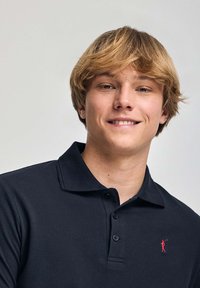 Marinblå pikétröja i bomull med klassisk krage, tre-knappslösning och en liten röd logotyp på vänster bröst.