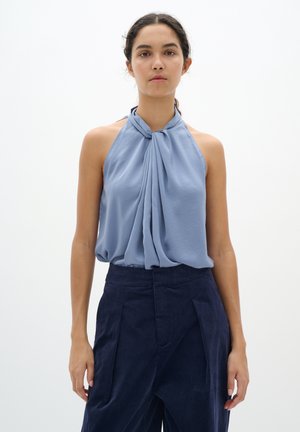 Himmelblaues ärmelloses Blusenshirt mit einem geknoteten Design am Ausschnitt, glatter Textur und drapiertem Stoff, kombiniert mit hochtaillierten marineblauen Hosen.