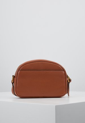 Sac besace en cuir marron avec dessus arrondi, finition texturée, poche avant plate et ferrures latérales dorées sur surface blanche.