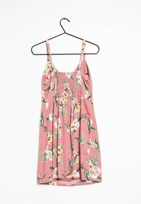 Różowa sukienka na lato w kwiaty z cienkimi ramiączkami, marszczonym gorsetem i marszczonym dołem. Ozdobiona białymi i żółtymi kwiatami oraz zielonymi liśćmi, wykonana z lekkiego materiału.