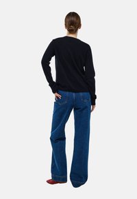 Pull noir à manches longues, associé à un jean en denim bleu à jambes larges. Les jeans comportent des poches à rabat et des coutures visibles.