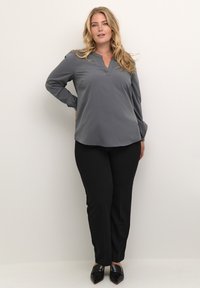 Grey long-sleeve blouse with a notch collar, paired with black tailored pants and sleek black slip-on shoes. Smooth fabric with minimal detailing.