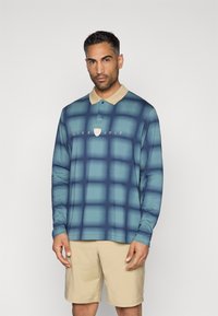 Πολυάσπρο πουκάμισο μακρυμάνικο σε γαλάζια κλίμακα με καρό σχέδιο, διαθέτοντας μπεζ γιακά και λογότυπο Nike Golf στο κέντρο.