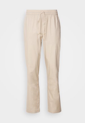 Beige Hose mit lockerer Passform, elastischem Bund und Kordelzug. Glatte Textur, leicht schmal zulaufendes Bein und keine sichtbaren Muster oder Metallteile.