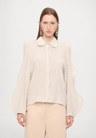 Lys beige knap-up skjorte med et struktureret stof, oversized puffede ærmer og en blød krave, parret med blege bukser.
