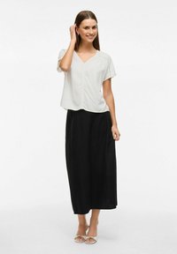 Blusa grigia chiara a maniche corte con scollatura a V, abbinata a una gonna nera lungo caviglia. La blusa ha una vestibilità rilassata e una texture morbida.