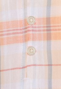 Chemise à manches courtes à carreaux dans des couleurs pastel claires, comprenant des rayures blanches, orange et grises. Boutons transparents et tissu doux avec texture détaillée.