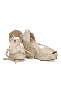 Sandalias de cuña beige con puntera abierta y correa al tobillo, que presentan tejido trenzado y una plataforma de yute texturizado. Interior de ante suave y diseño que proporciona soporte.
