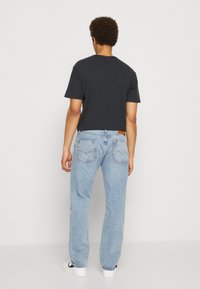 Camiseta negra de algodón de manga corta combinada con jeans de mezclilla azul claro. Los jeans tienen un corte clásico y bolsillos traseros con una etiqueta de logo.