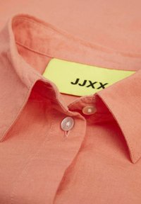 Korallenfarbenes Hemd mit Knopfleiste aus leichtem Stoff, ausgestattet mit einem klassischen Kragen, zwei Knöpfen und einem sichtbaren gelben Etikett mit dem "JJXX"-Logo.