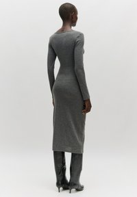 Langärmliges, tailliertes graues Kleid aus einem weichen Stoff, das bis zur Wade reicht, kombiniert mit schwarzen kniehohen Stiefeln mit spitzer Zehe.